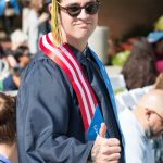 Young man wearing sunglasses in graduation regalia and wearing the Veteran stole giving a thumbs up.