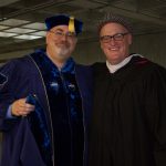 Craig Goralski wearing his blue academic regalia with another man in academic regalia.