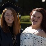 Young lady with graduation gown and cap with another young lady with long red hair and black and white polka dot blouse.
