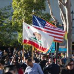 American and California flag flying amid commencement crowd.