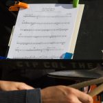 Music sheets on a stand with two hands holding drumsticks.
