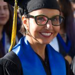 A young lady with glasses and wearing her cap and gown, smiling during commencement.