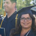 A young lady with glasses and wearing her cap and gown, smiling during commencement.