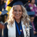 A young lady with blond hair wearing graduation regalia and EOPS stole .