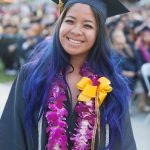 A young lady wearing graduation regalia and purple leis.