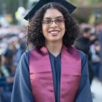 A young lady with short hair and glasses wearing graduation regalia.