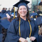 A smiling young lady with brown hair wearing graduation regalia.