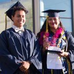 Smiling young man and young lady holding an award, in cap and gown.