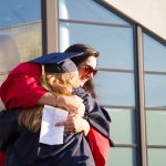 Two women in graduation regalia, embracing.