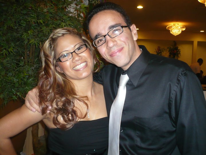 Man and woman smile at camera, both wearing glasses and black dress clothes
