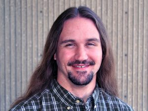 Man with long hair, smiling, wearing plaid shirt