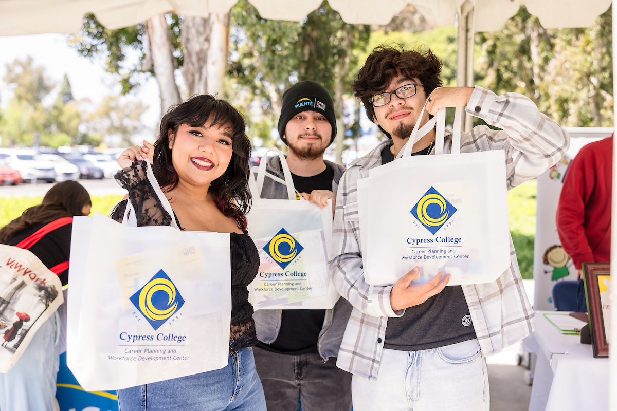 Three smiling students hold Cypress College bags while they pose for the camera