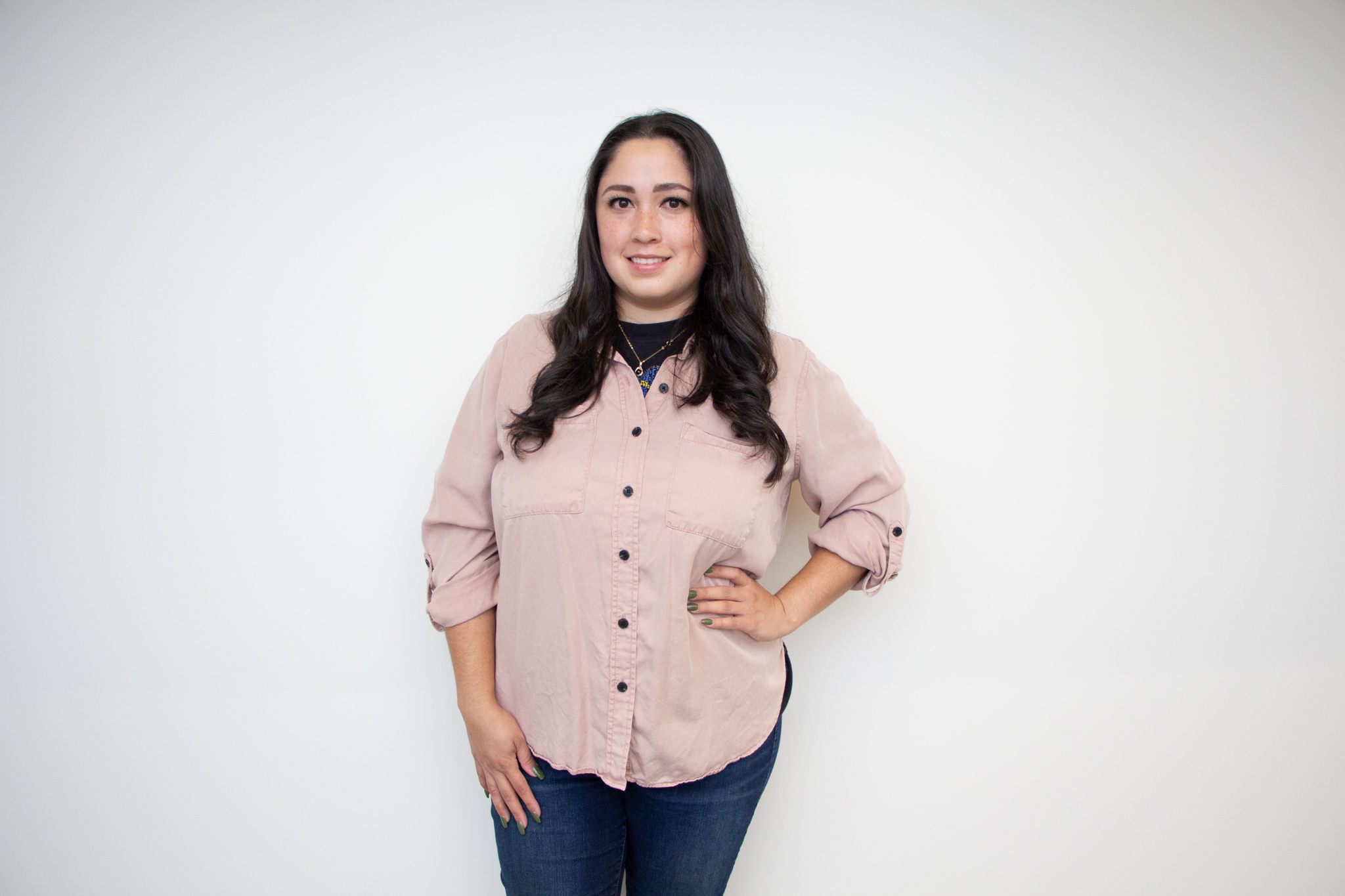 Geraldine Lopez wears a blush-colored button-down shirt in front of a white wall. 
