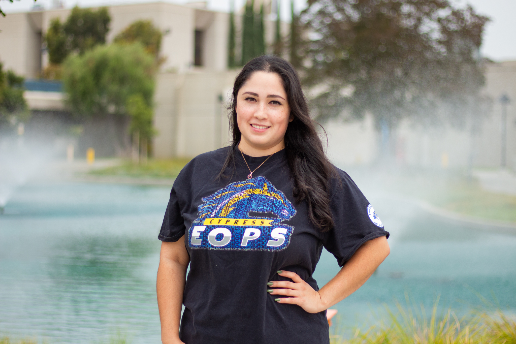 Cypress College student Geraldine Lopez stands in front of the campus pond wearing an EOPS t-shirt. 