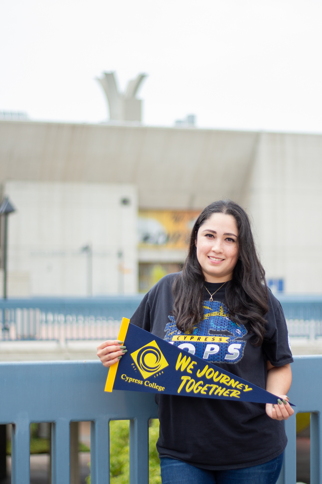 Student Geraldine Lopez holds a "We journey together" pennant as she stands on the Cypress College second-level piazza. 