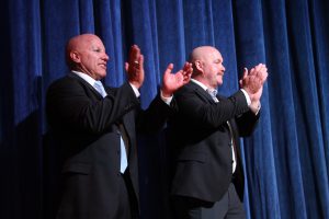 Two men in suits applauding.