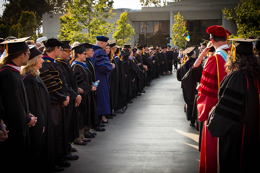 Faculty and Administration in commencement regalia standing to form a pathway for students to walk through