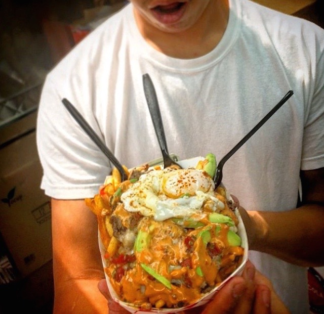Person in white t-shirt holding a plate of nacho fries
