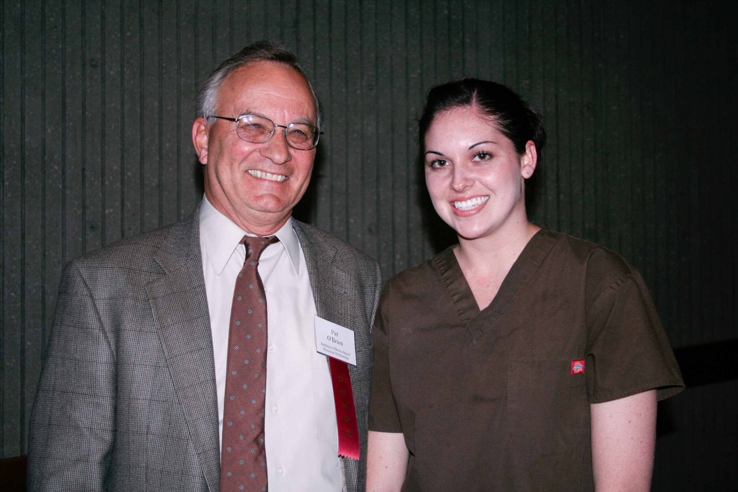A man in a coat and tie with a "donor" tag hanging from his name badge stands with a student