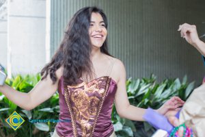 Young lady with long brown hair wearing a brown and gold top.