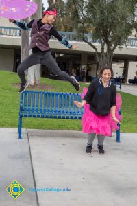 Young man jumping in the air holding a paper umbrella and a young lady wearing a pink tutu.