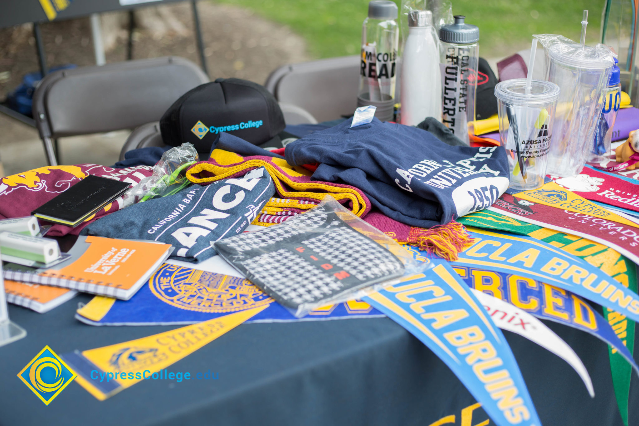 Various pennants, t-shirts, water bottles, cups and notebooks from UC and Cal State campuses.