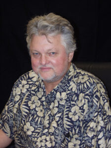 Portrait of a man with grey hair and a goatee. He is wearing a Hawaiian shirt.