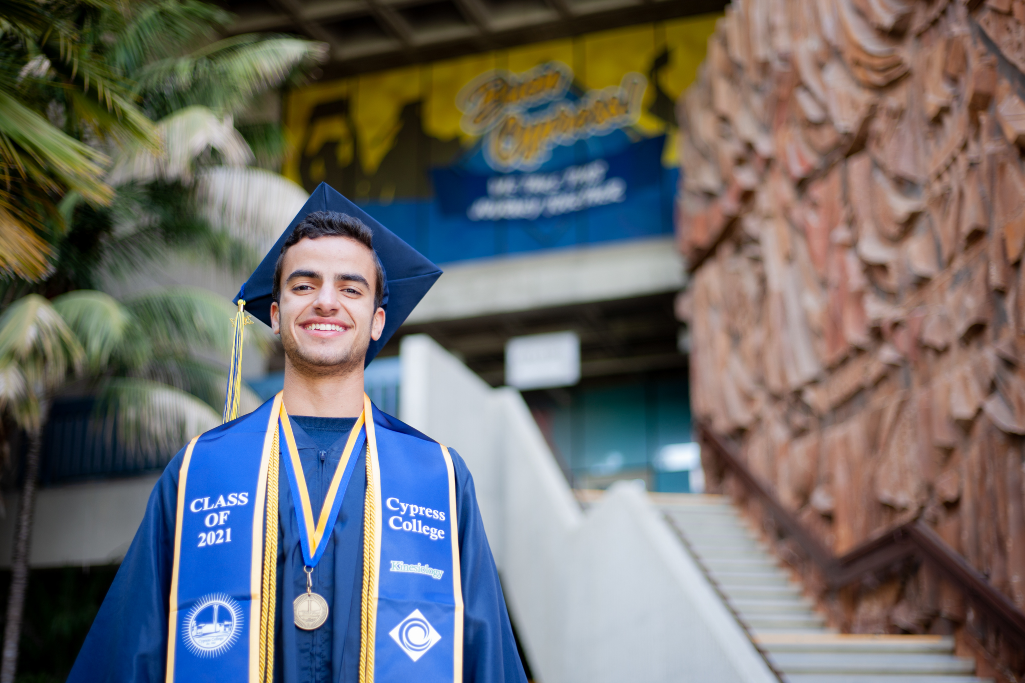 Kinesiology student Jonathan Gad poses in graduation regalia in front of College Complex building. 