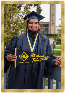 Student Abdul Meelar stands in graduation regalia in front of Gateway Plaza with green grass and buildings in background.