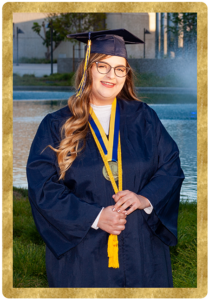 Student Krystal Kosacki wears graduation regalia and poses in front of campus pond.