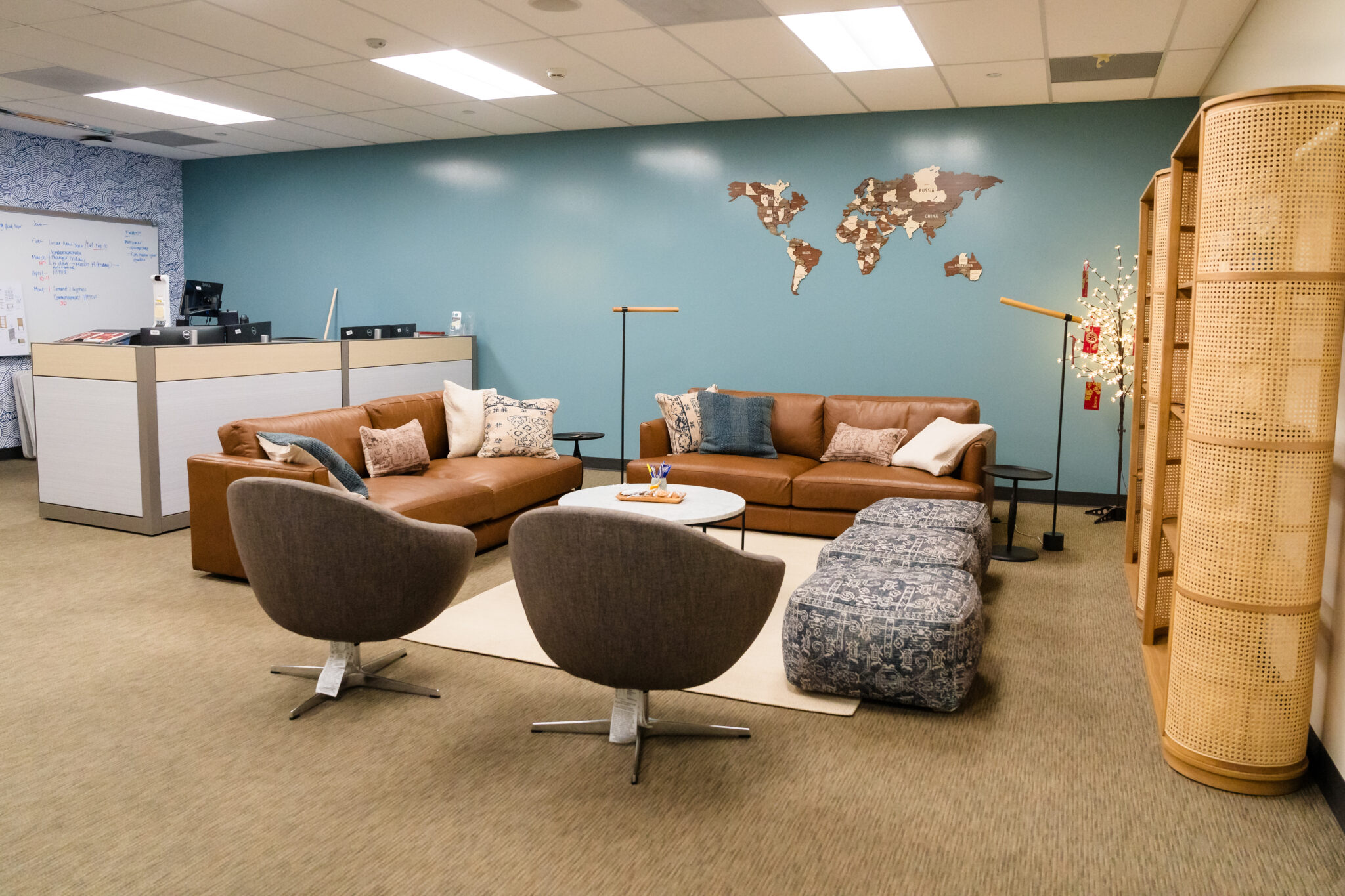 Office lounge area with brown leather sofas, two gray swivel chairs, and a blue ottoman. A map decorates the teal wall. A desk with a computer is in the corner.