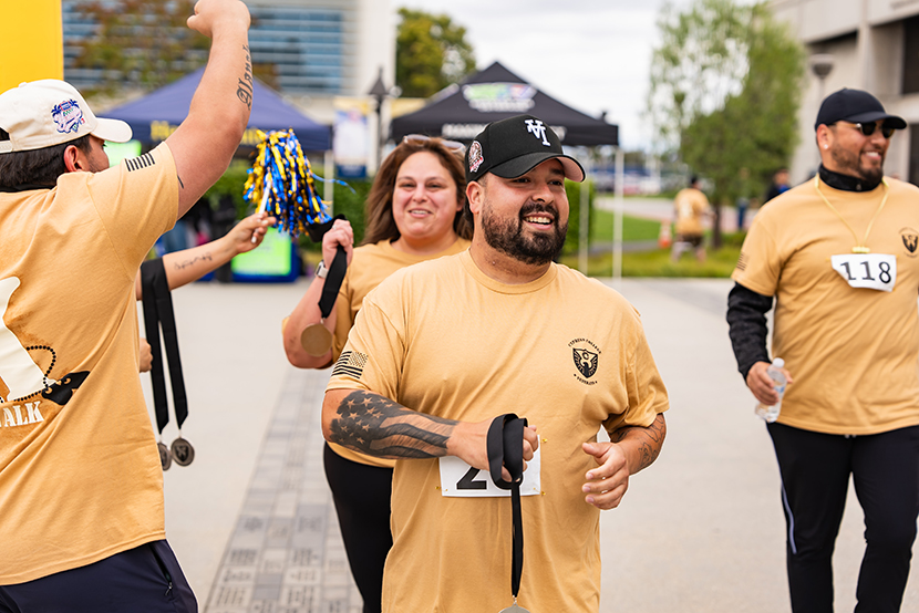 A man crossing the finished with medal in hand, in the background is two more finishing participants and a person cheering them on