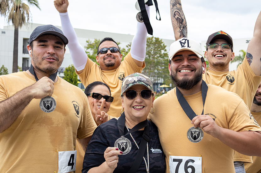 Group of people at a 5k race, three people are showing off their medals and the two behind them holding up their arms