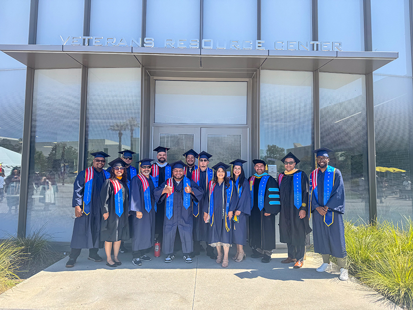 A group of graduates in their cap and gown in front of the Veterans Resource Center