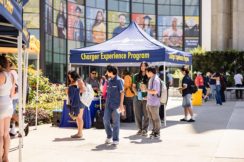 A diverse group of individuals strolls through a campus, surrounded by colorful tents set up for an event.