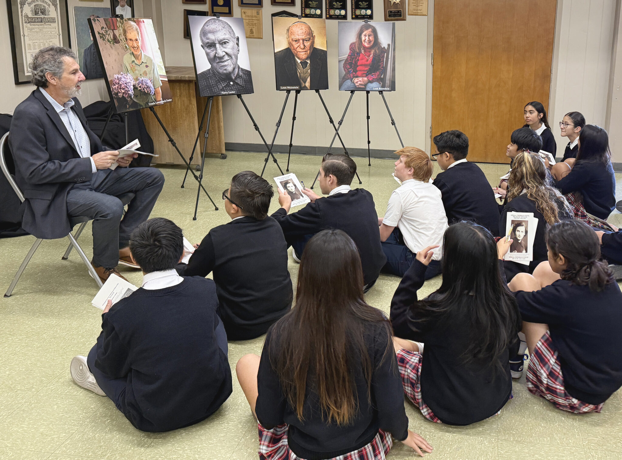 Catholic-school students sit attentively while listening to a man share about Holocaust survivor photographs.