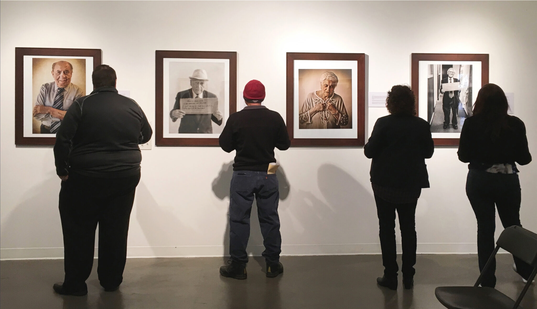 Visitors admire framed photographs on a gallery wall, showcasing various individuals and their stories.