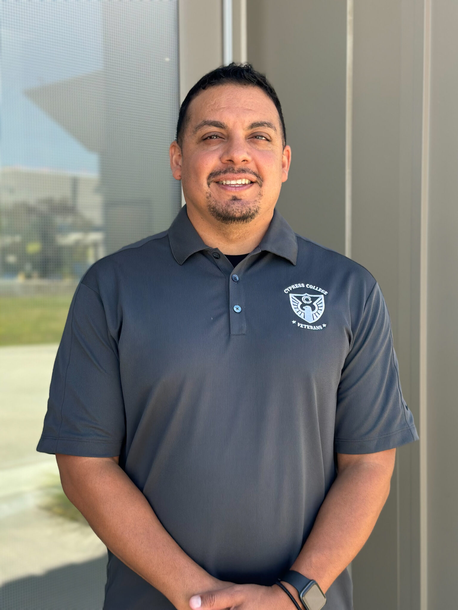 Carlos Martinez, Student Services Technician, wearing a gray Cypress College Veterans polo shirt, standing in front of the VRC