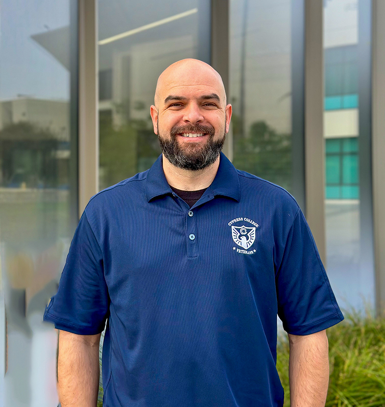 Nick Gutierrez, Student Services Coordinator, wearing a navy blue Cypress College Veterans polo shirt with the VRC in the background