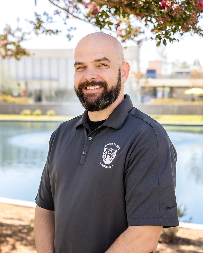 Nick Gutierrez, Student Services Coordinator, wearing a navy blue Cypress College Veterans polo shirt with the VRC in the background
