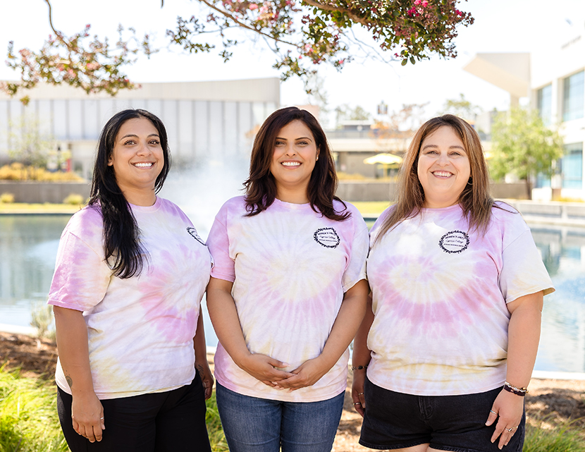 Women's Unit(y) 2025-26 Leadership: Natalie Navarette, Esmeralda Martin, Aneth Kirk. Each woman is wearing a pink tie-dyed shirt.