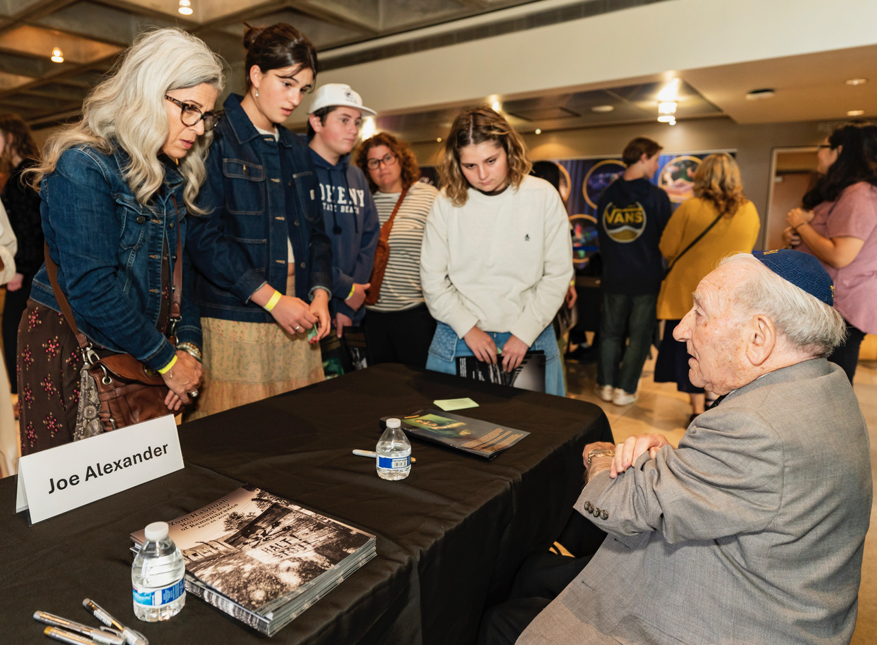 Survivor Joe Alexander shares the tattoo he got on his arm when he was in Auschwitz Concentration Camp. Students listen intently.