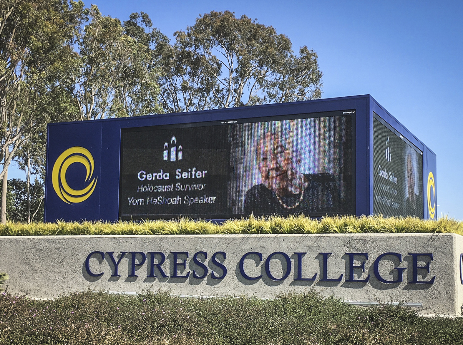 Digital billboard at Cypress College featuring Gerda Seifer, Holocaust survivor and Yom HaShoah speaker, with smiling portrait.
