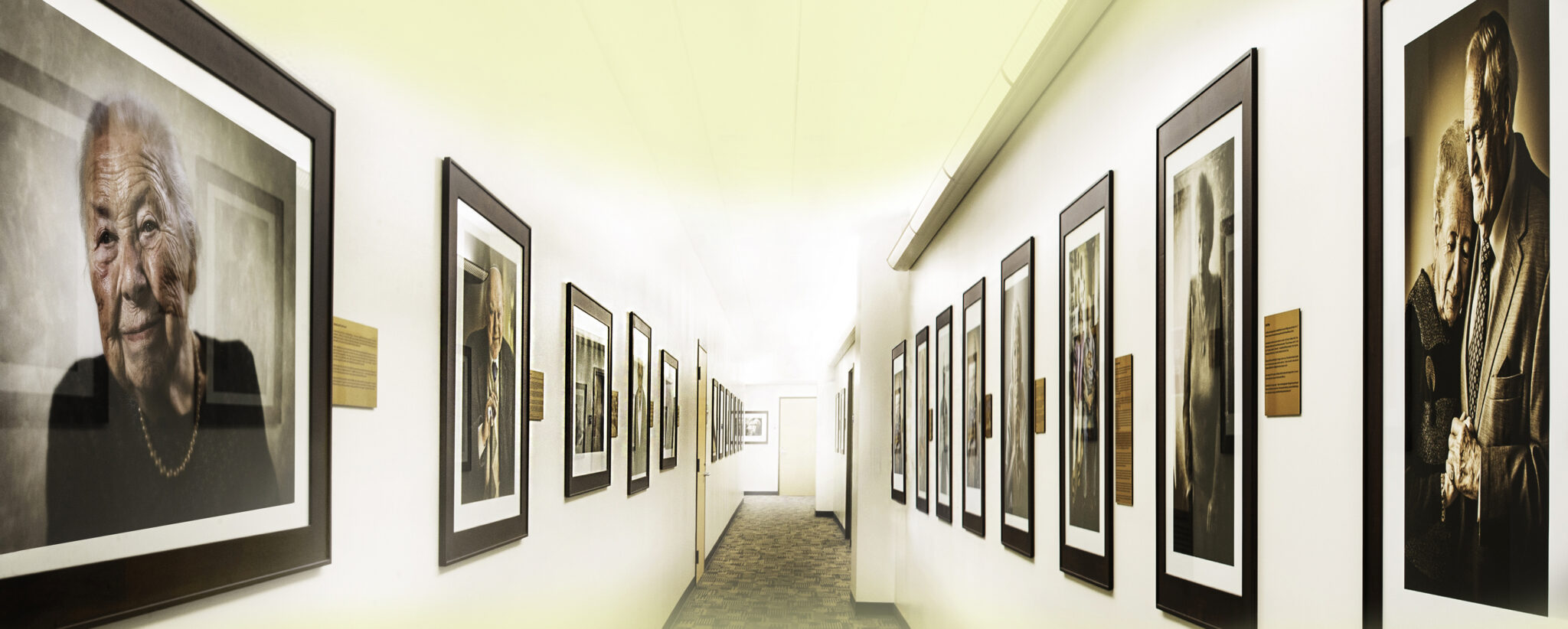 A hallway lined with framed photographs of various people, showcasing diverse expressions and moments captured in time.
