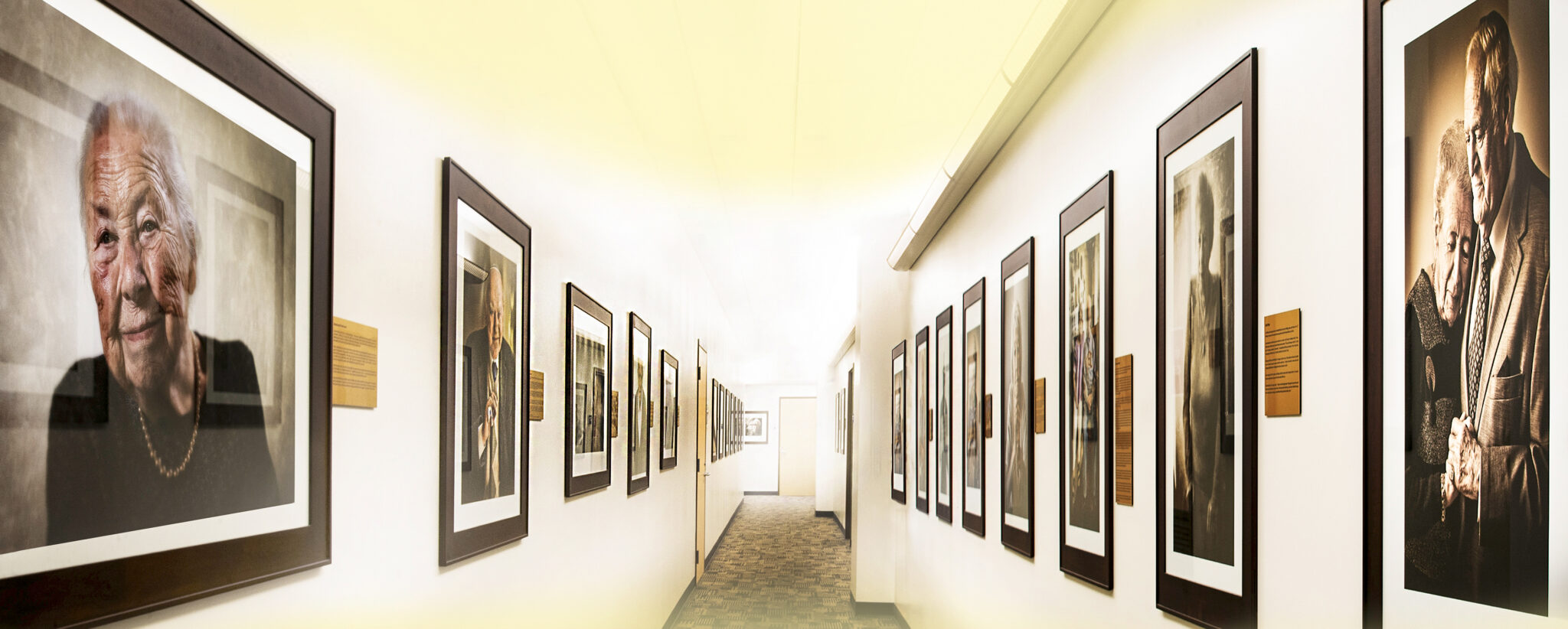 A hallway lined with framed photographs of various people, showcasing diverse expressions and moments captured in time.