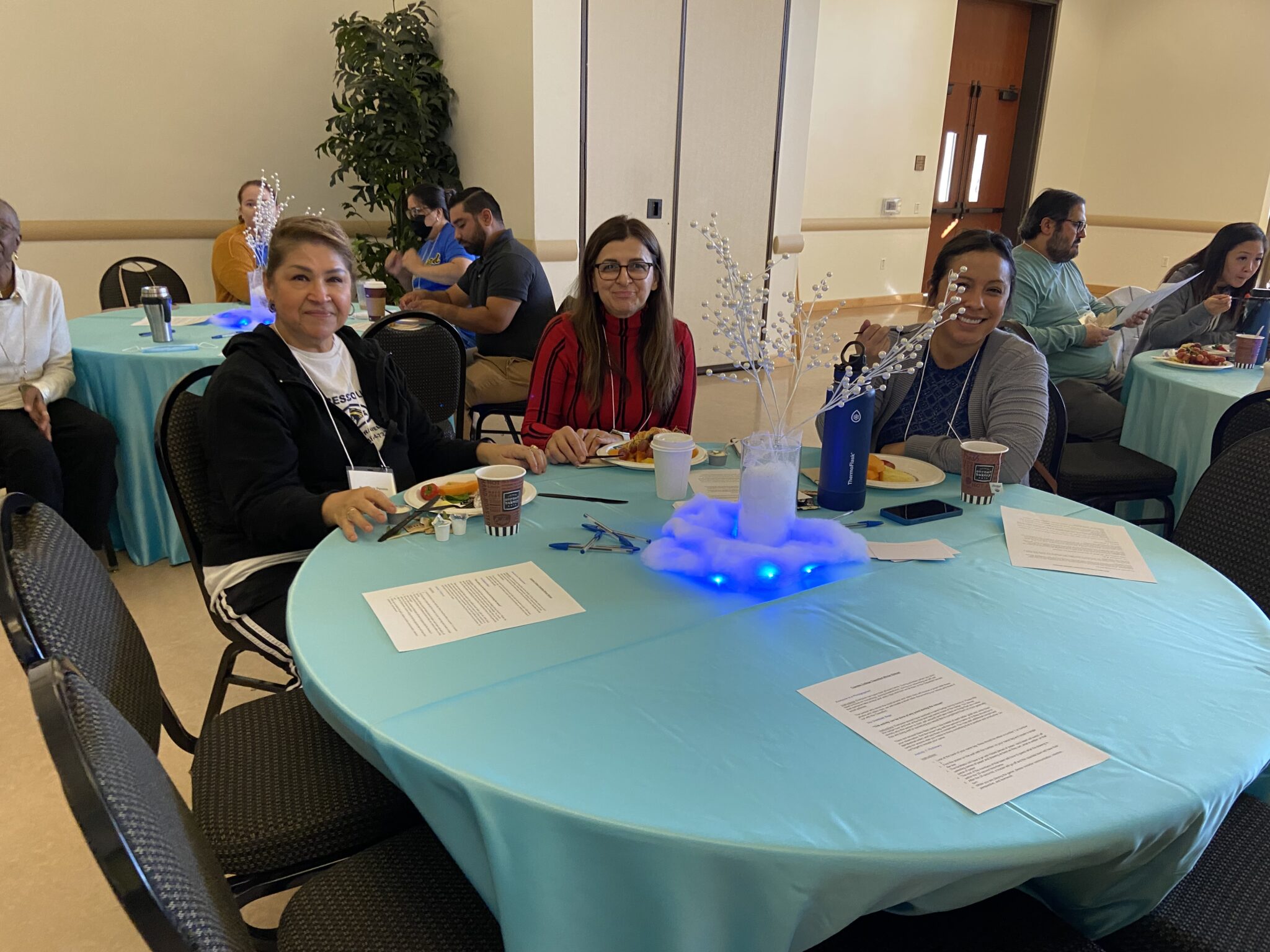 Three classified staff take a photo together at their table while enjoying their breakfast pastries.