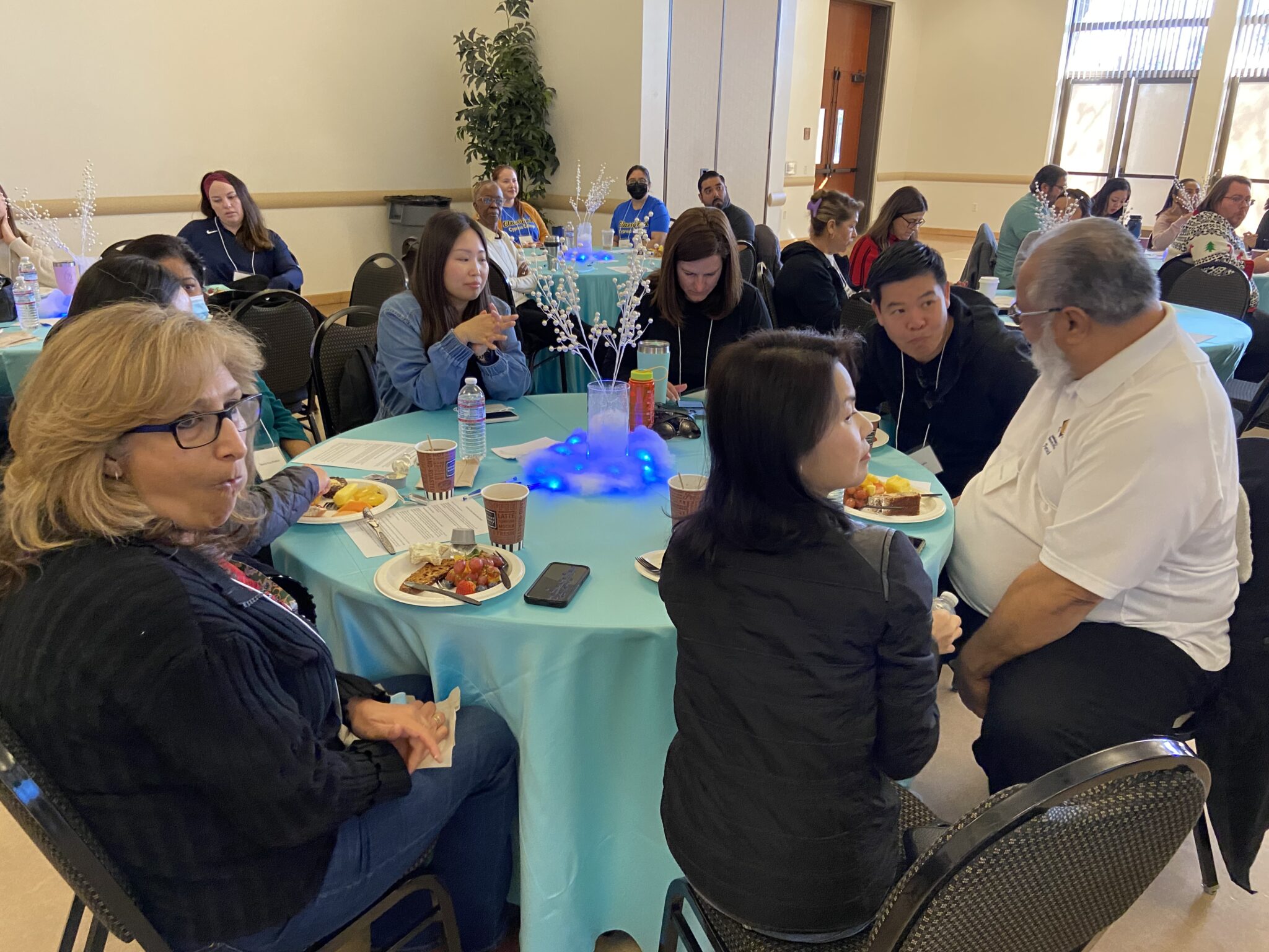 A group of classified staff listening to directions and presentation while eating breakfast.