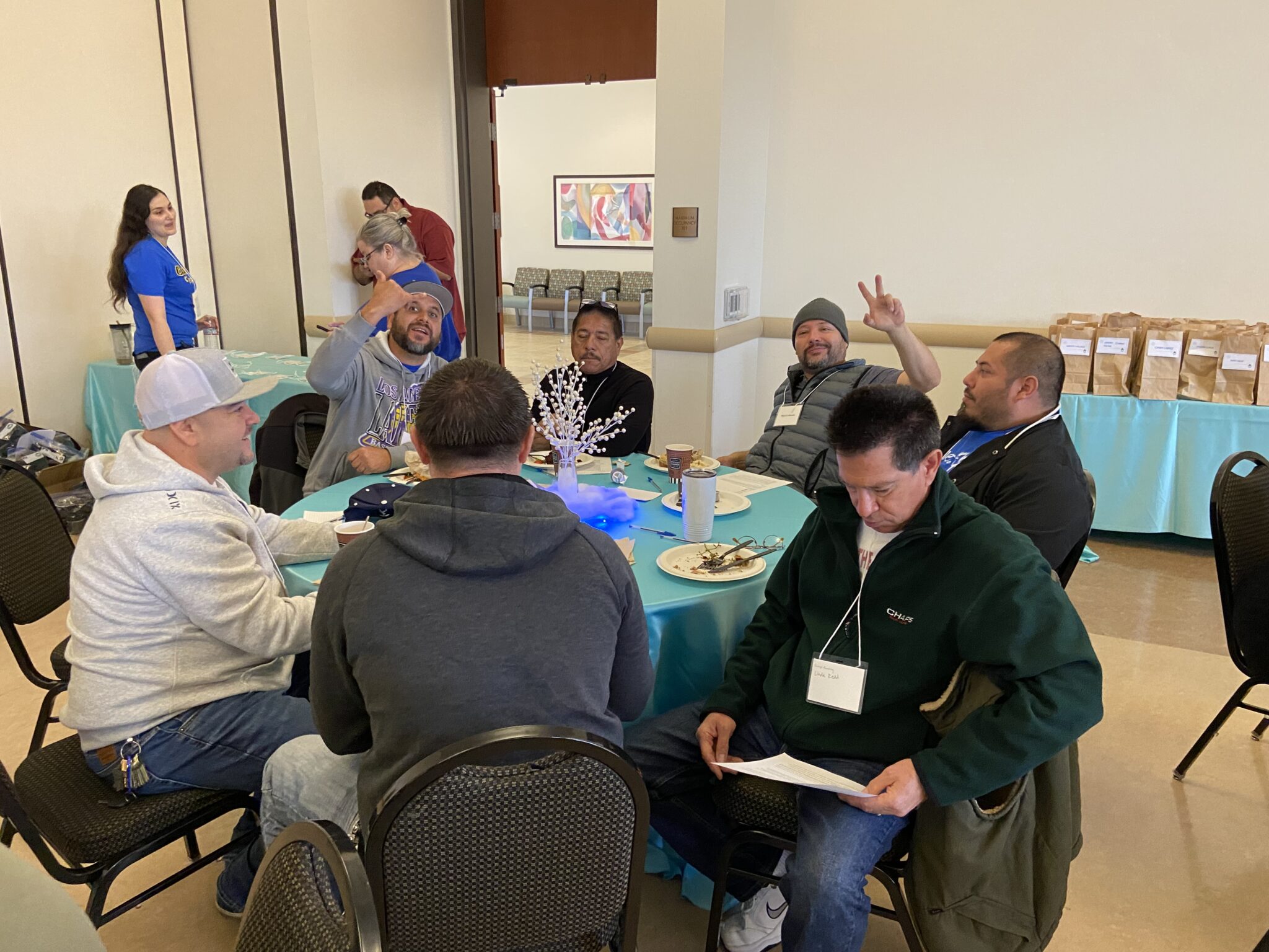 A group of classified staff are sitting at a table reviewing activity directions with two staff members showing their peace symbols.