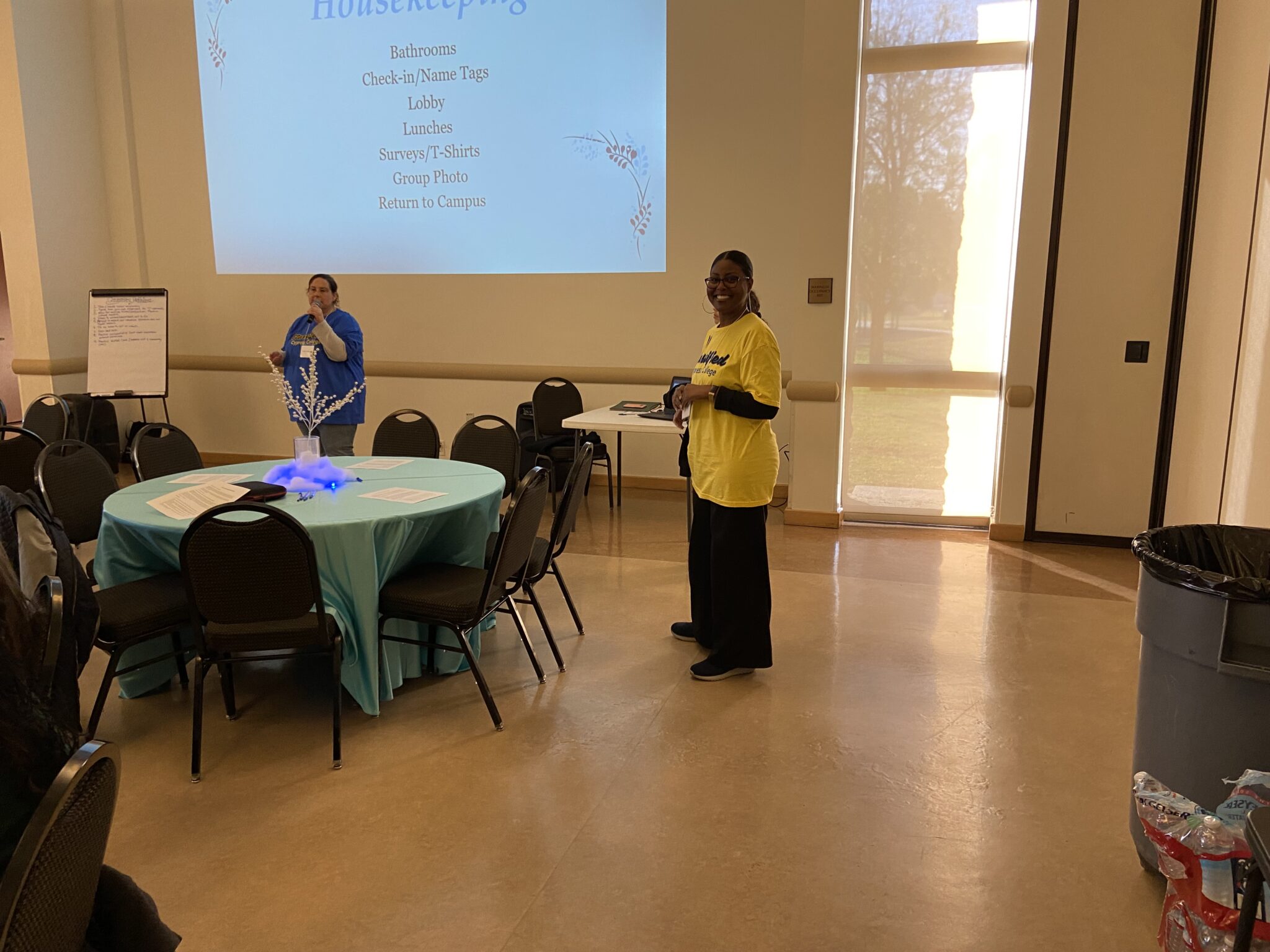 A classified senate board member presenting to the group and another board member smiling for a photo in a yellow shirt.