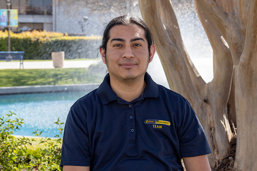 Dual Enrollment staff J. Miguel Flores-Garcia with blue shirt and pond in background